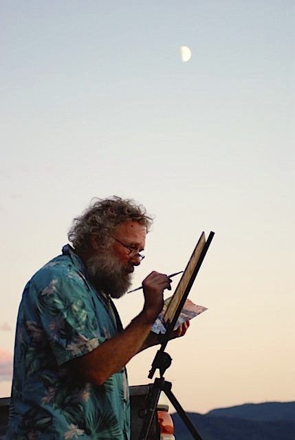 Peter Corbett painting against an easel with the moon in the sky and mountains in the background